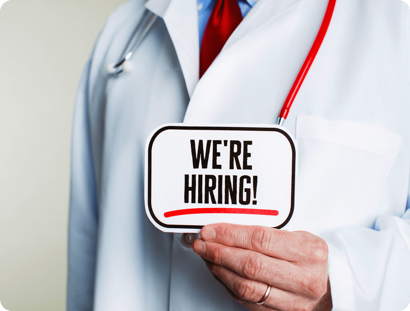 Here's an alt tag for the image: Doctor holding "We're Hiring!" sign.
